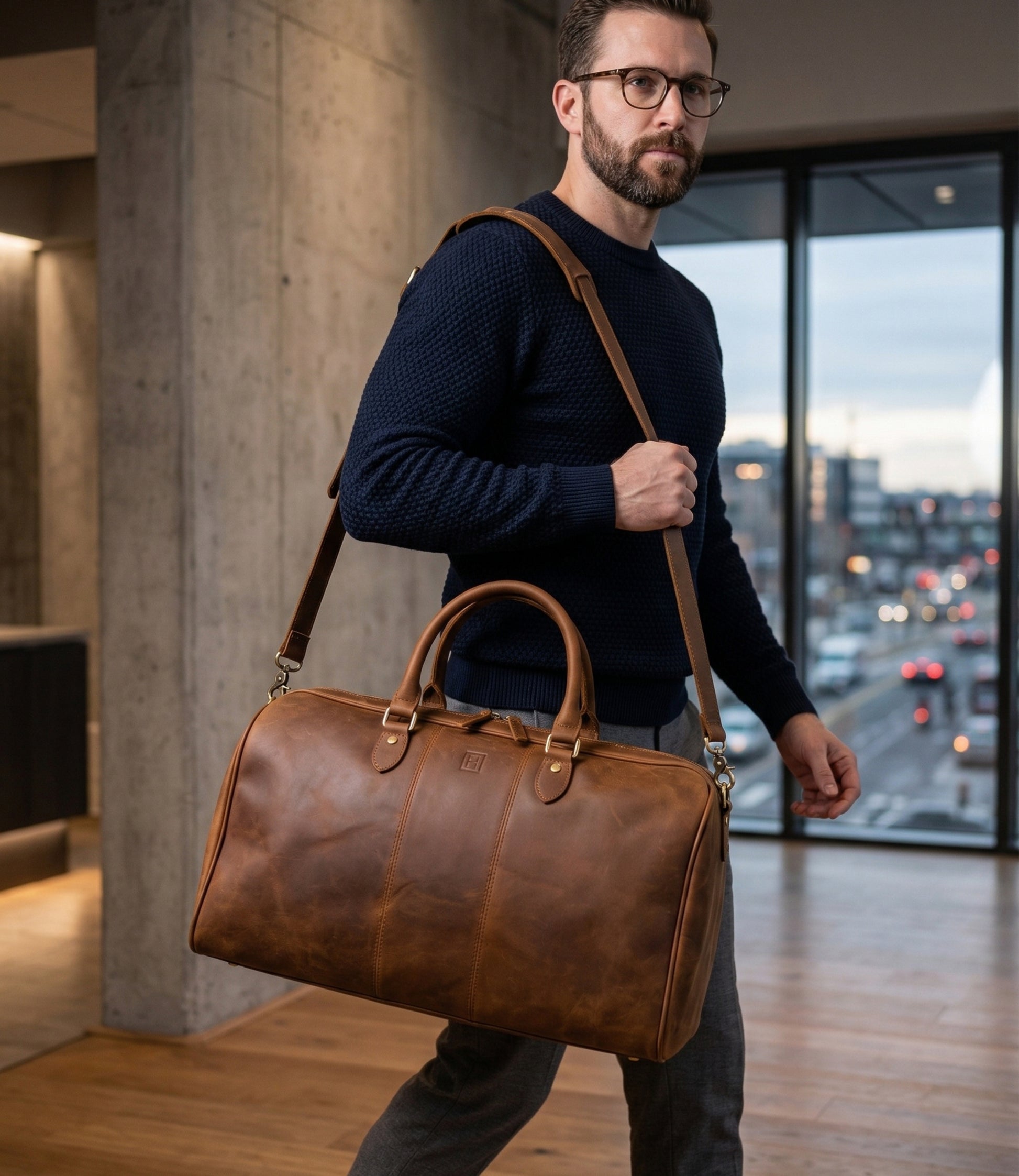 Man carrying a brown leather duffel bag in an indoor setting with a cityscape view.