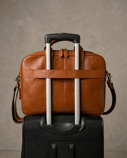 Brown leather briefcase with wheels on top of a black suitcase against a brown background